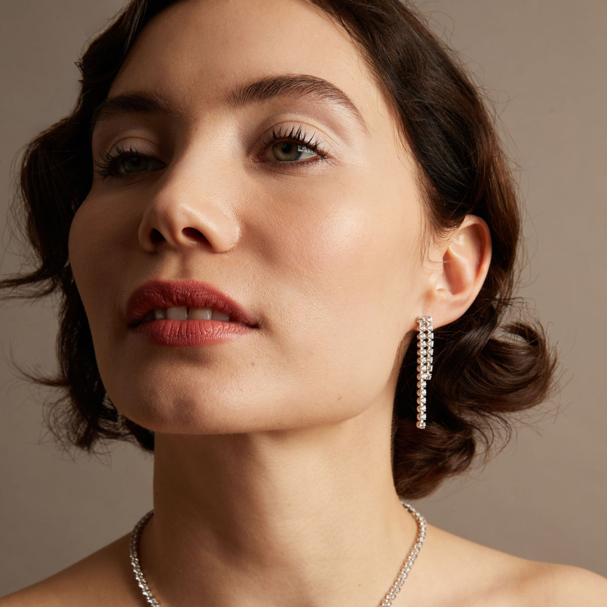 Model. Woman wearing tennis earrings with brown background.