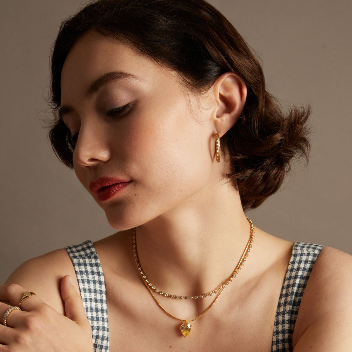 Model. Woman wearing gold hoop earrings and two necklaces.
