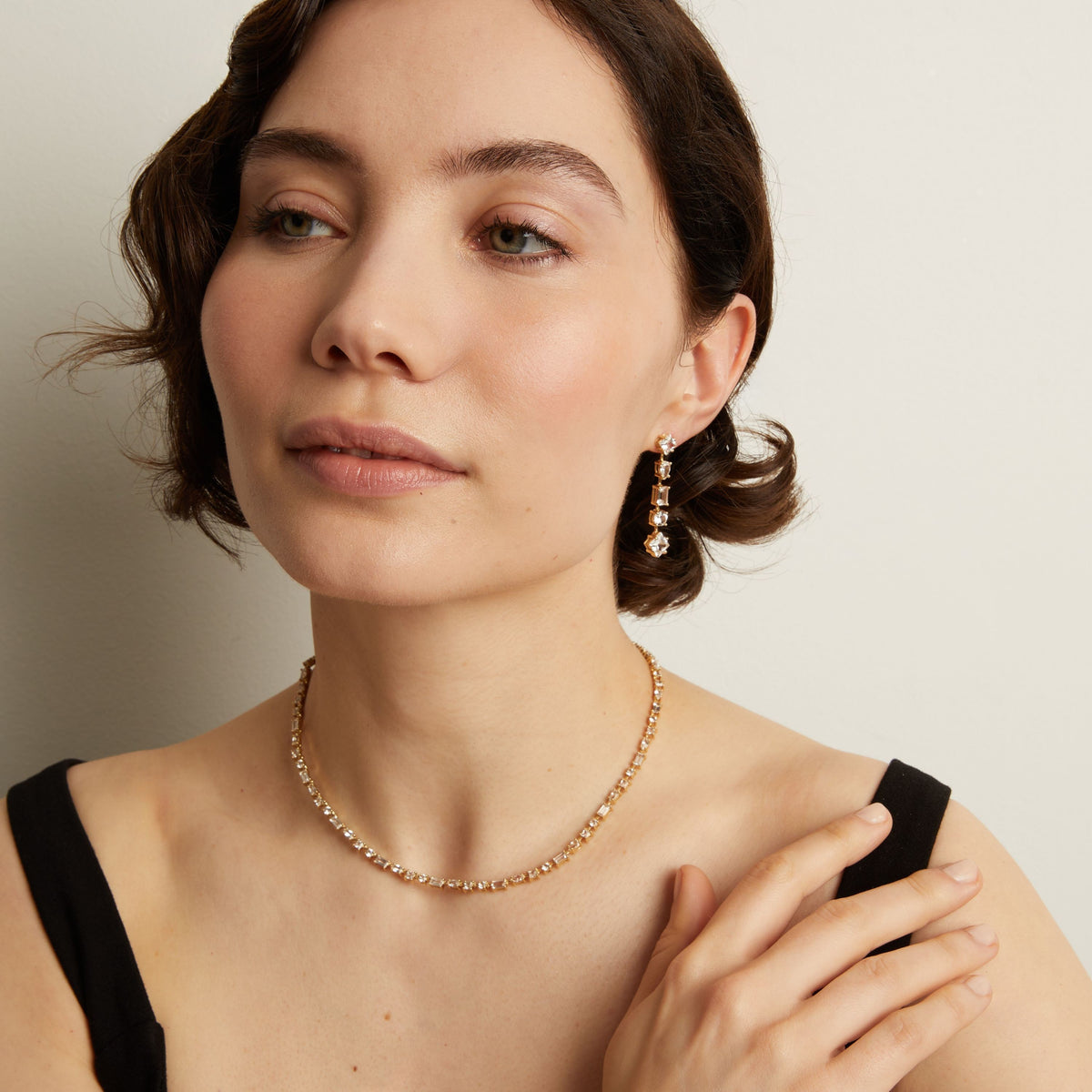 Model. Woman wearing a tennis necklace and earrings against a neutral background