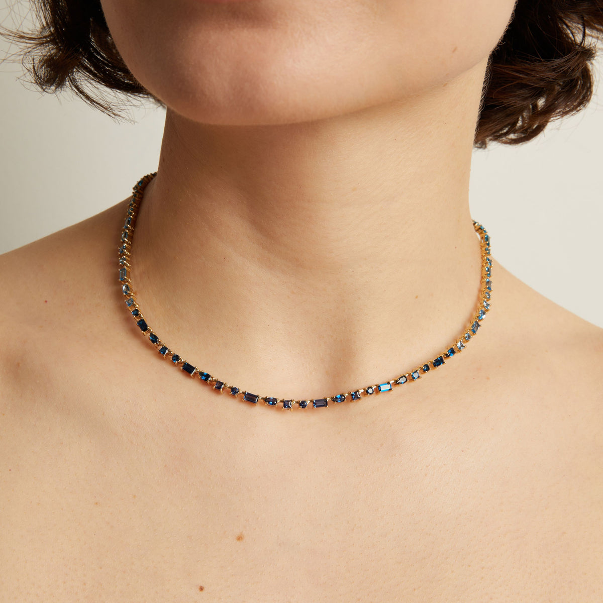 Blue tennis necklace worn by a person on a neutral background. Model