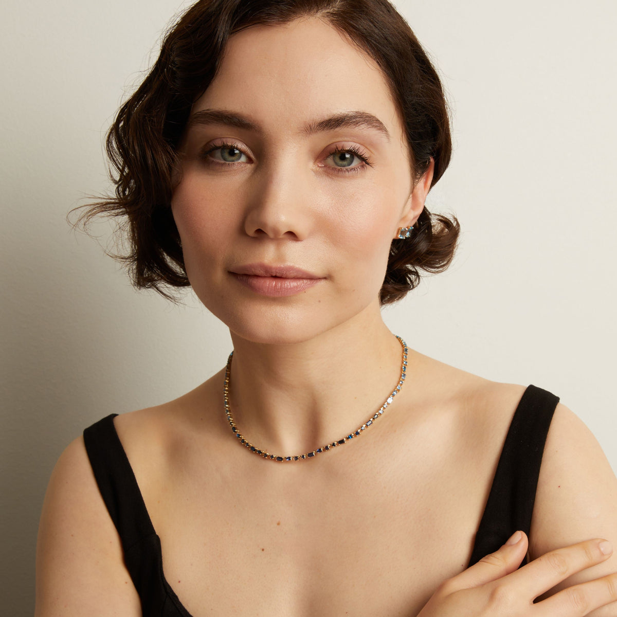 Woman wearing a blue tennis necklace against a neutral background. Model