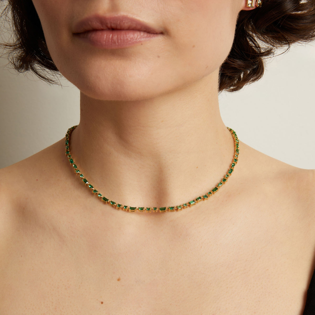 Close-up of a person wearing a green tennis necklace against a neutral background. Model