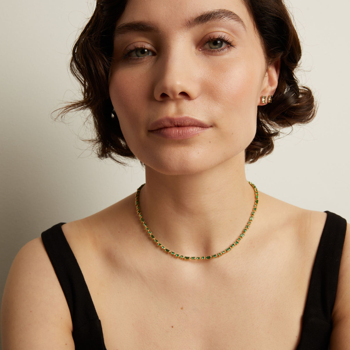 Woman wearing a green tennis necklace against a neutral background. Model