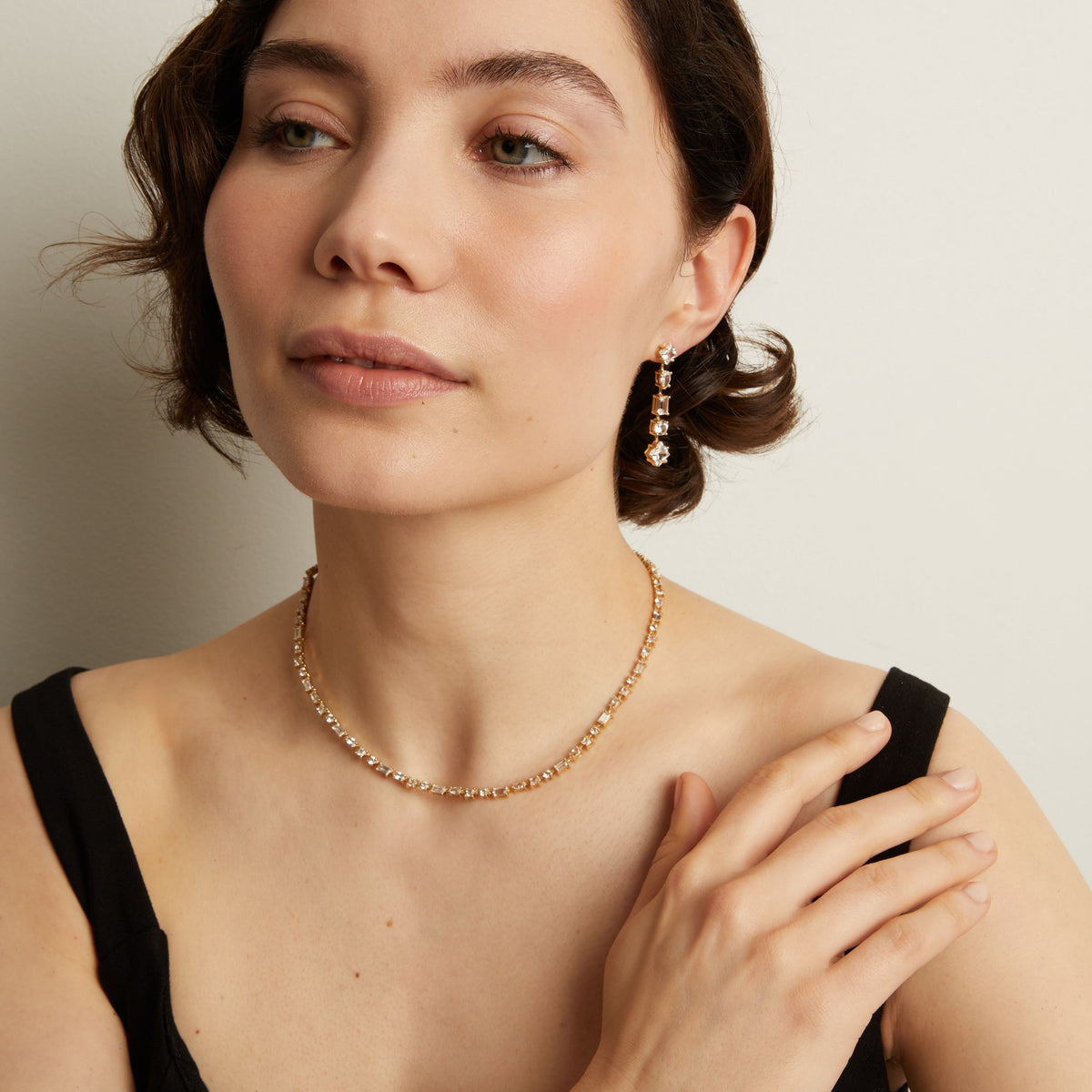 Model. Woman wearing a tennis necklace and earrings against a neutral background