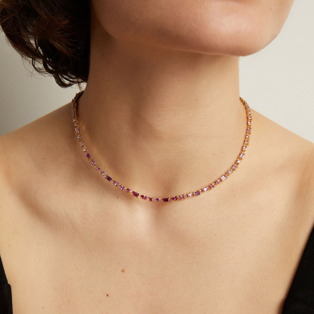 Pink tennis necklace worn by a person on a neutral background. Model