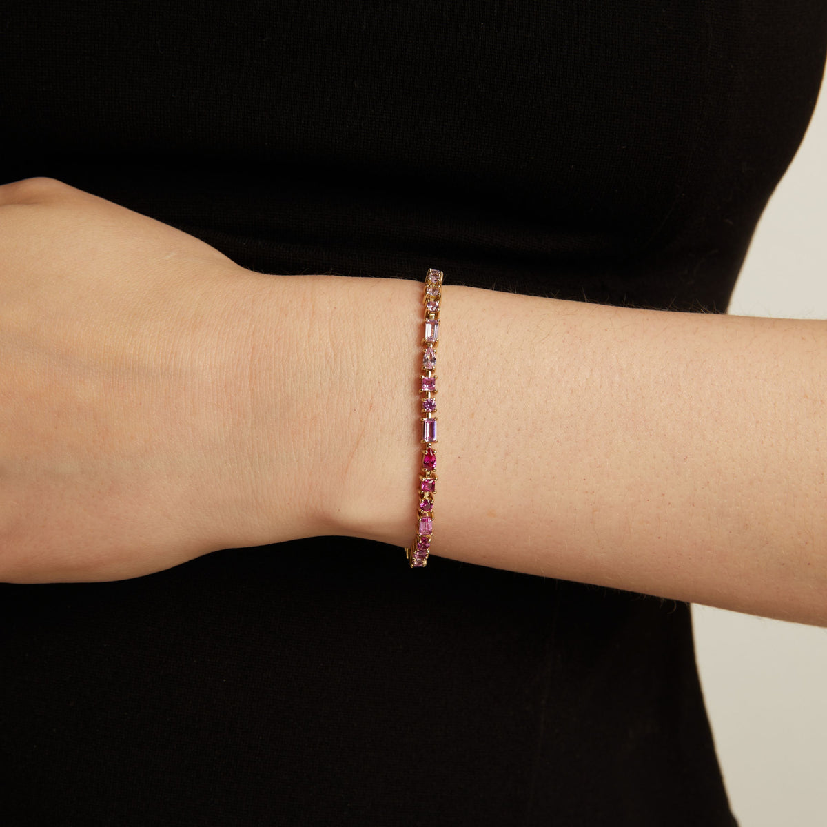 pink tennis bracelet on a wrist against a black background. Model