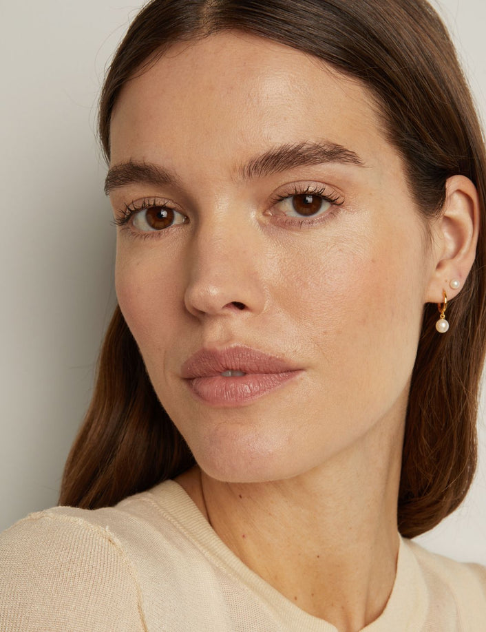 Model. Close-up of a woman wearing pearl earrings against a neutral background