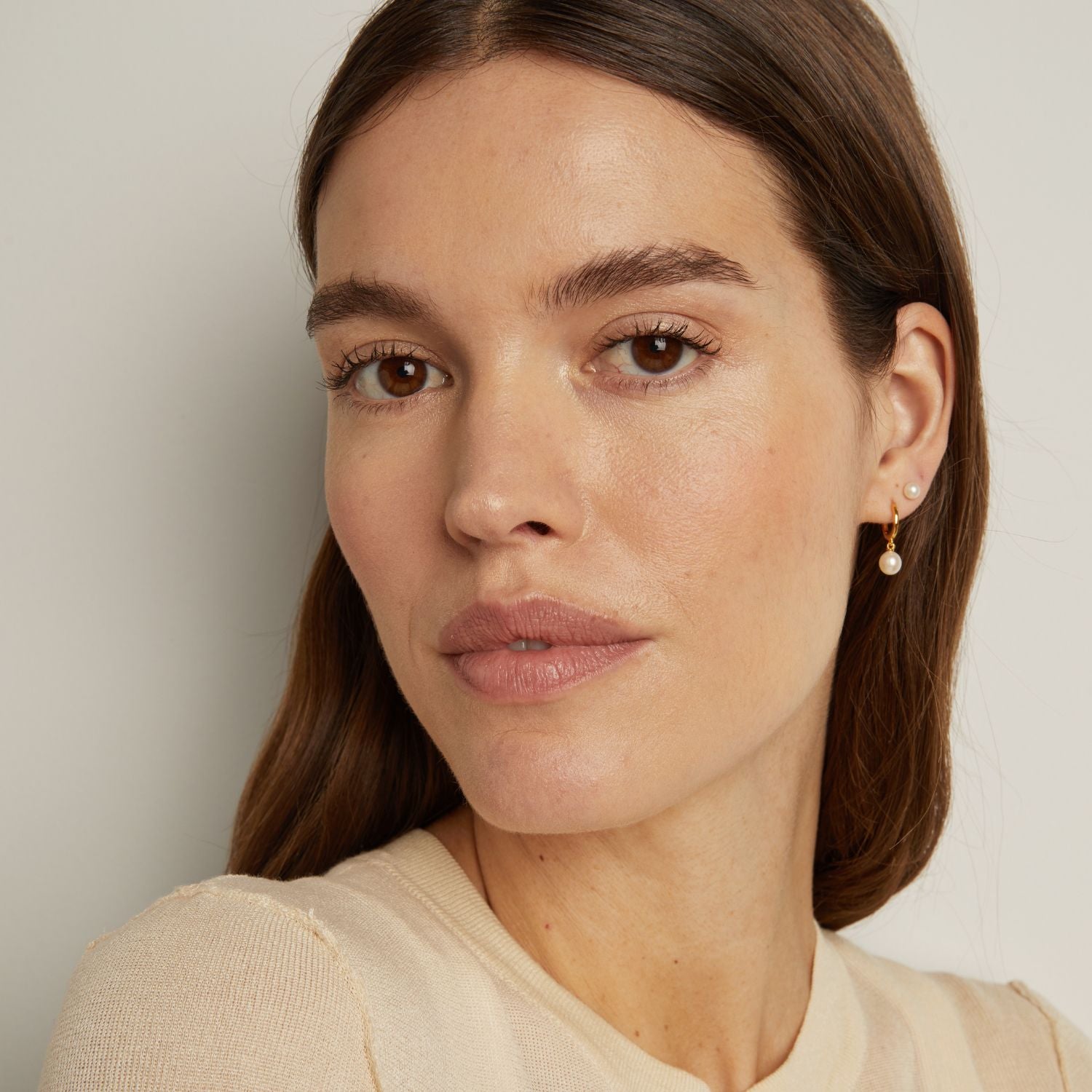 Model. Close-up of a woman wearing pearl earrings against a neutral background