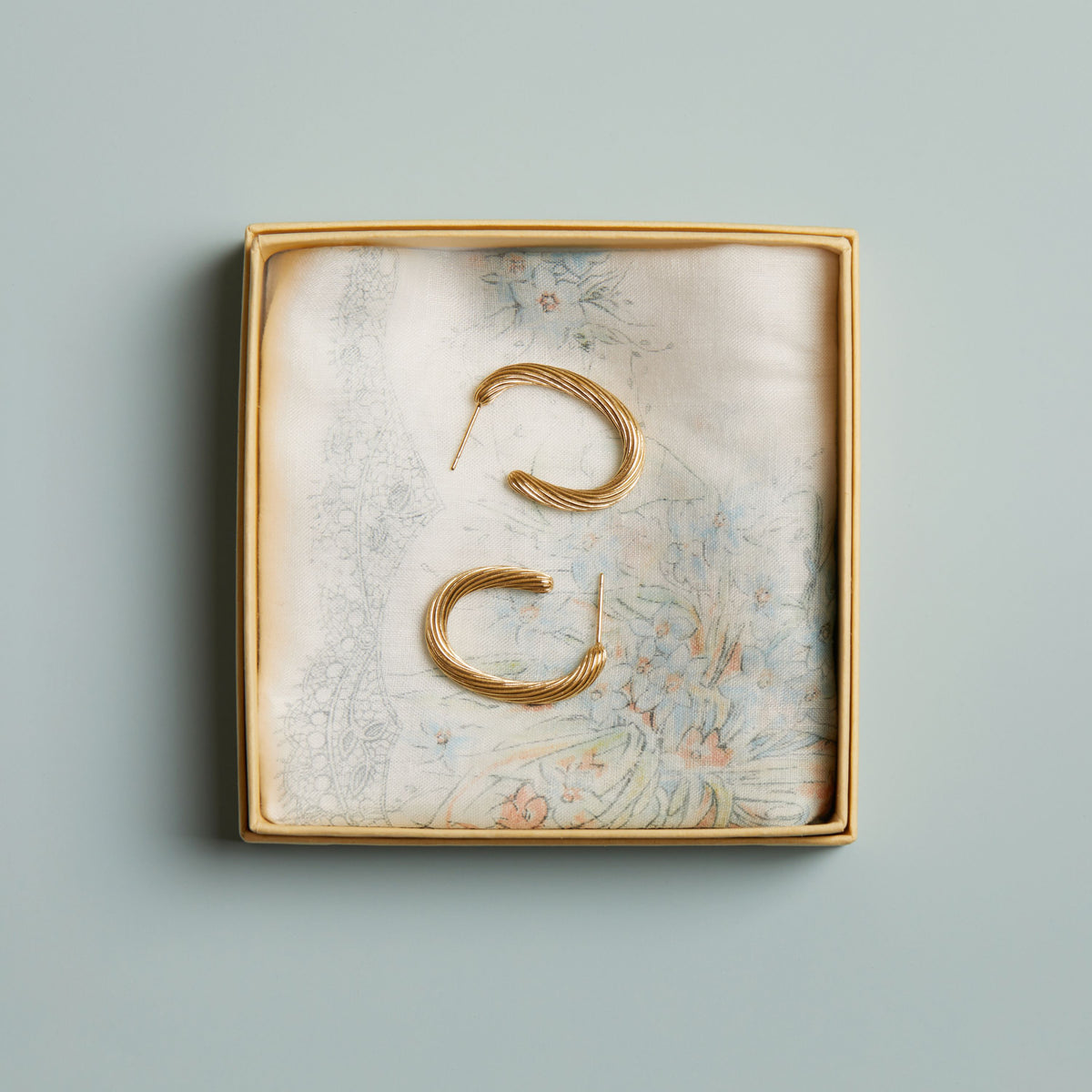 Model. Gold earrings in a decorative box on a blue background