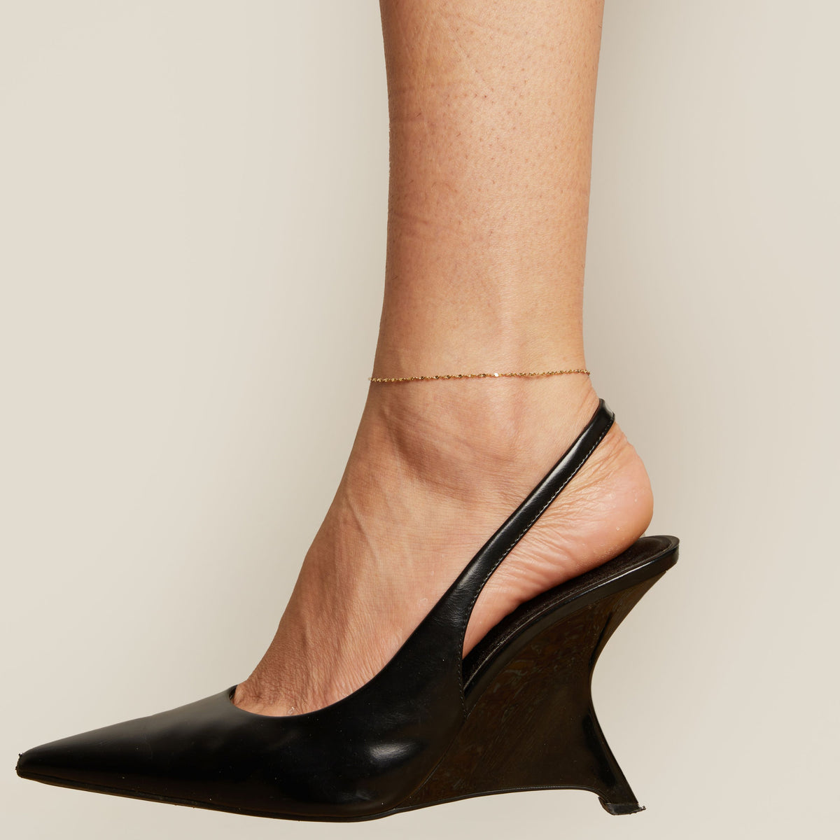  Black wedge heel shoe and anklet worn by a person on a neutral background
