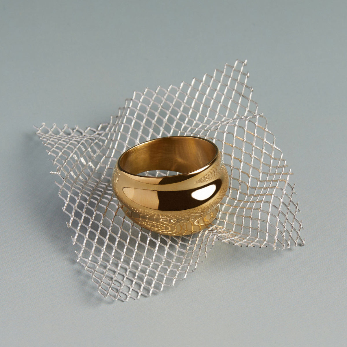 Model. Gold ring on a textured silver grid against a gray background