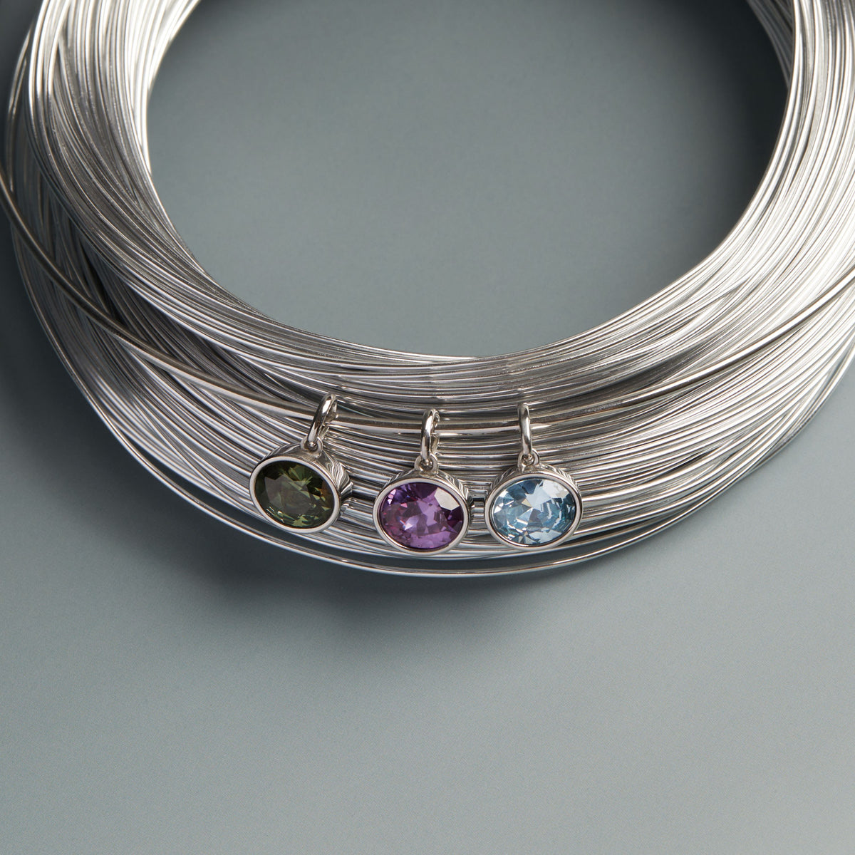 Model. Three gemstone pendants on silver wires against a gray background
