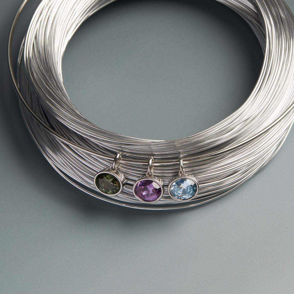 Model. Coiled silver wire with three gemstone pendants on a gray background