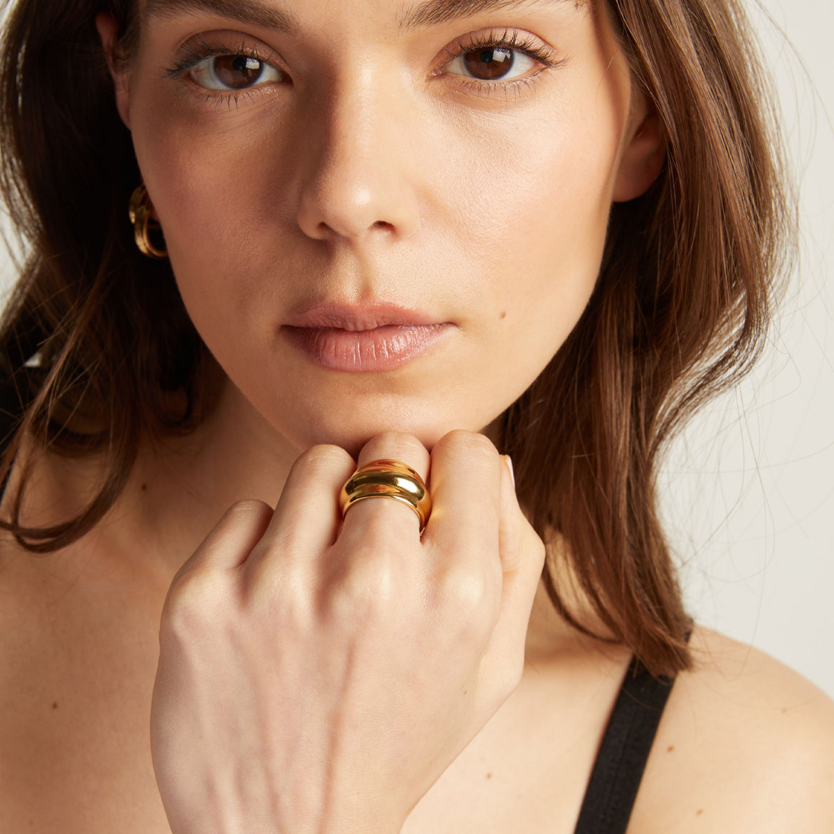 Close-up of a woman's hand wearing a gold ring with a neutral background.