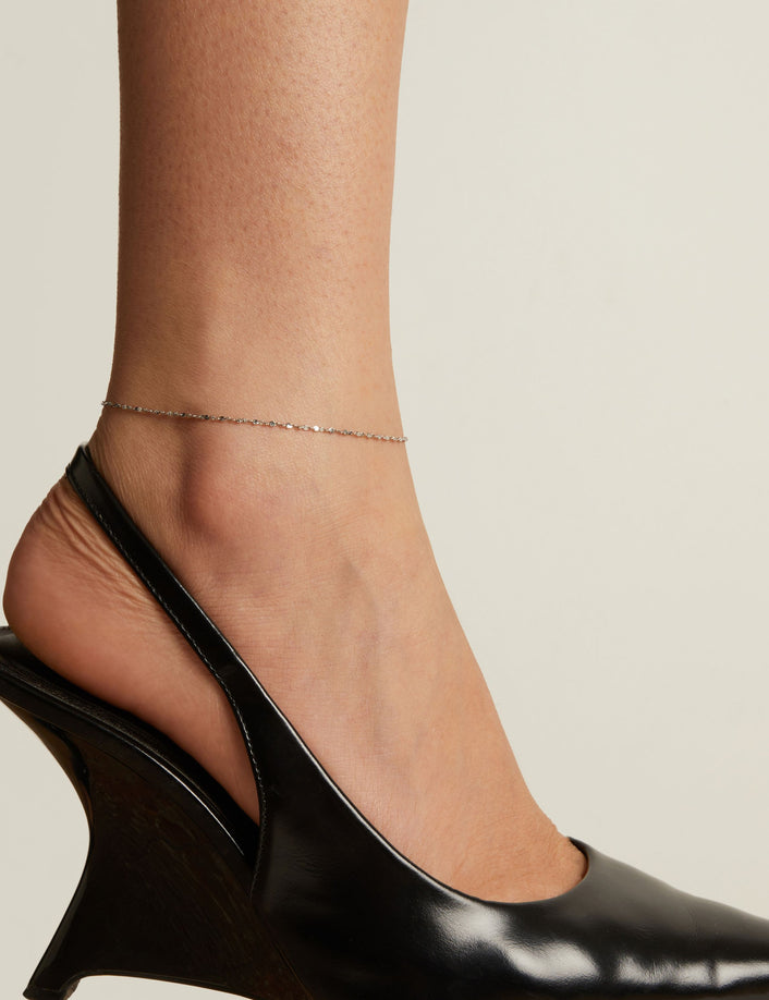 Model. Black wedge heel shoe and anklet worn by a person on a neutral background