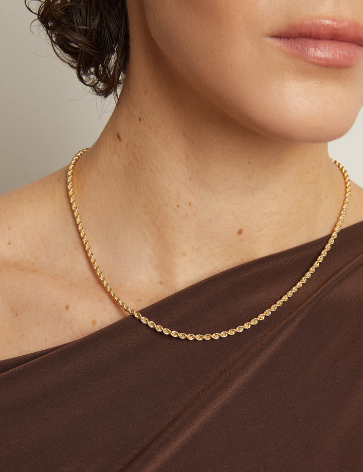 Model. Gold necklace worn by a person with a neutral background