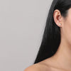 Video of woman wearing gemstone stud earrings on neutral background.