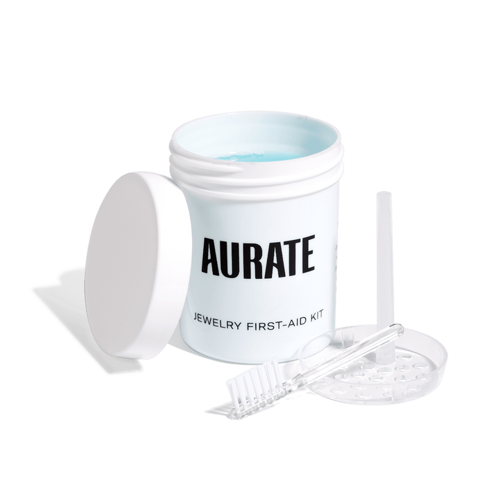 Model An open jar of the Aurate Jewelry First-Aid Kit, alongside its lid, a small brush, and a clear tray.